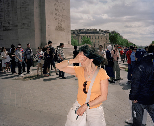 woman stand with her right hand covering her eyes and her left clenching a digital camera