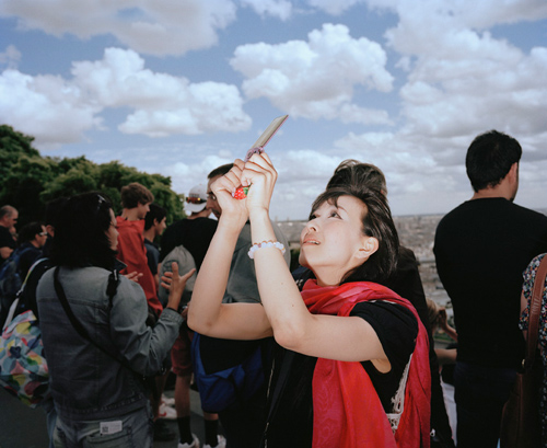 woman stand with her right hand covering her eyes and her left clenching a digital camera